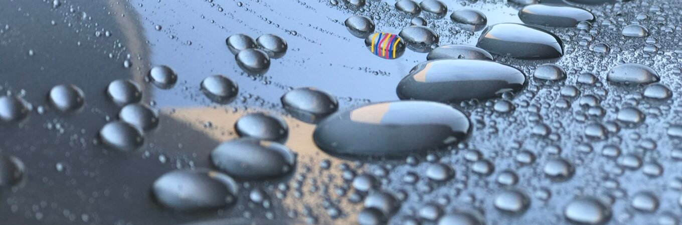 Water droplets beading on a car surface after a ceramic coating application. The coating provides a self-cleaning ability, encapsulating dirt and allowing it to roll off with the water.