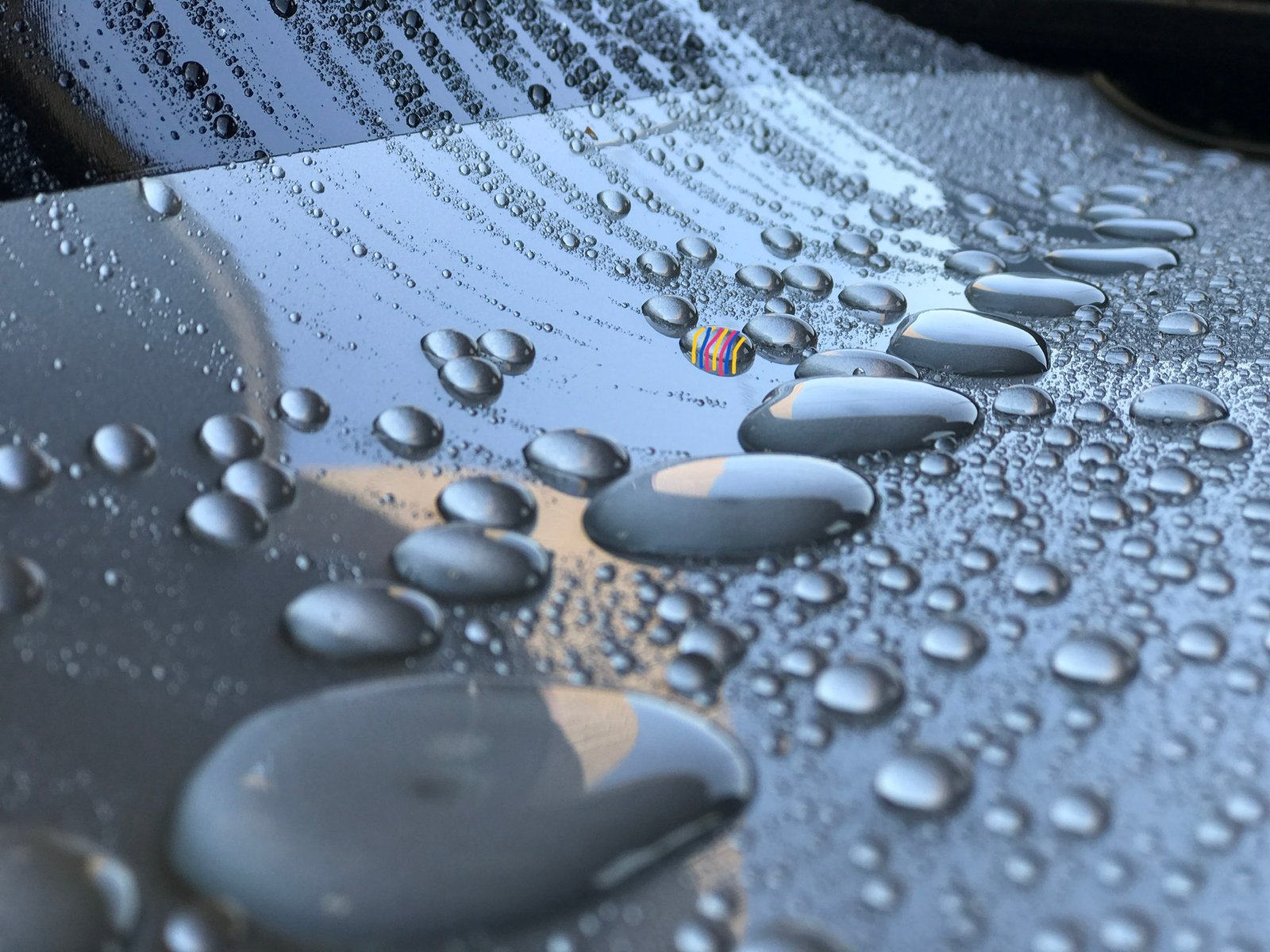 Water droplets beading on a car surface after a ceramic coating application. The coating provides a self-cleaning ability, encapsulating dirt and allowing it to roll off with the water.